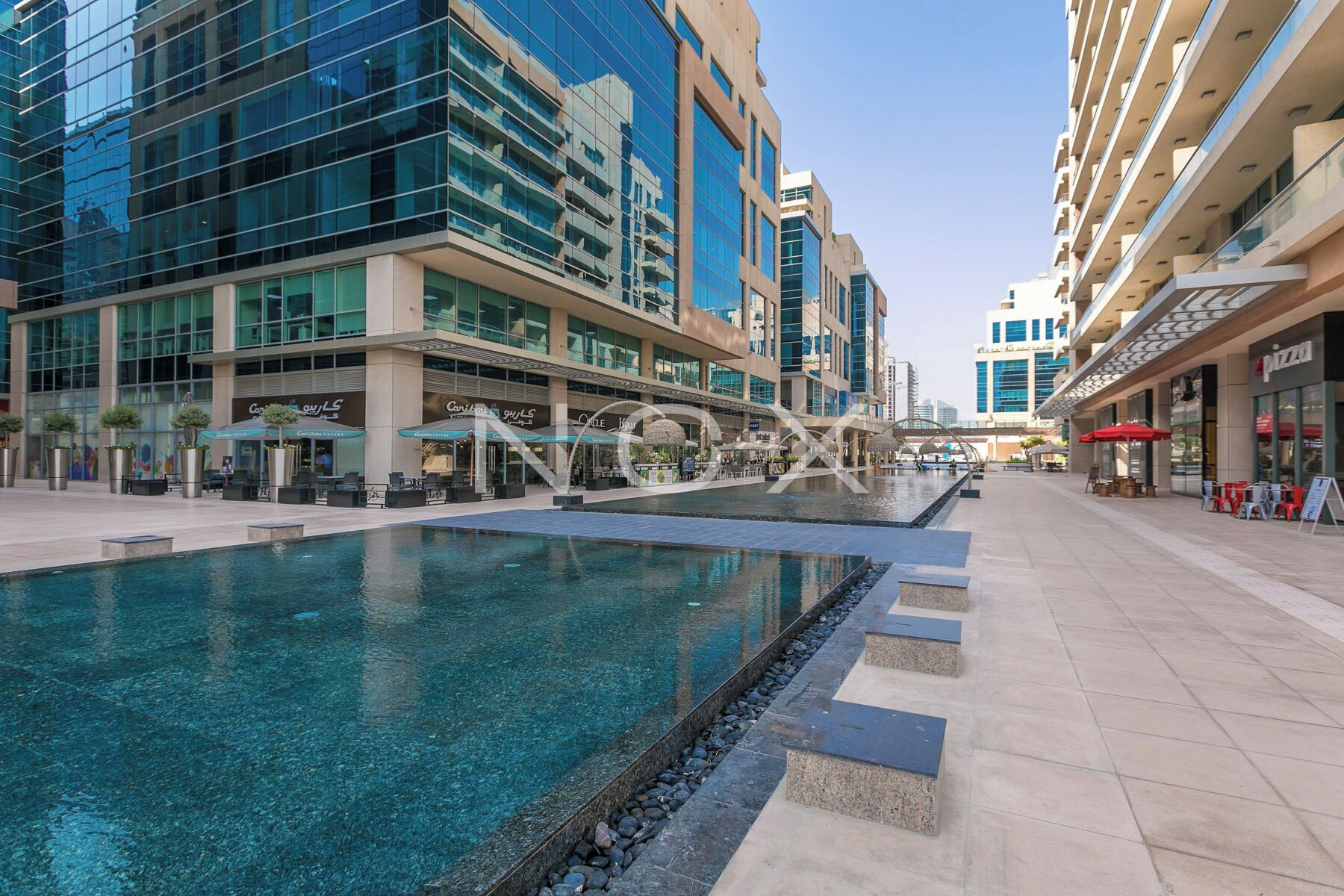 A modern hotel with a central pool, outdoor seating, and a variety of dining options.
