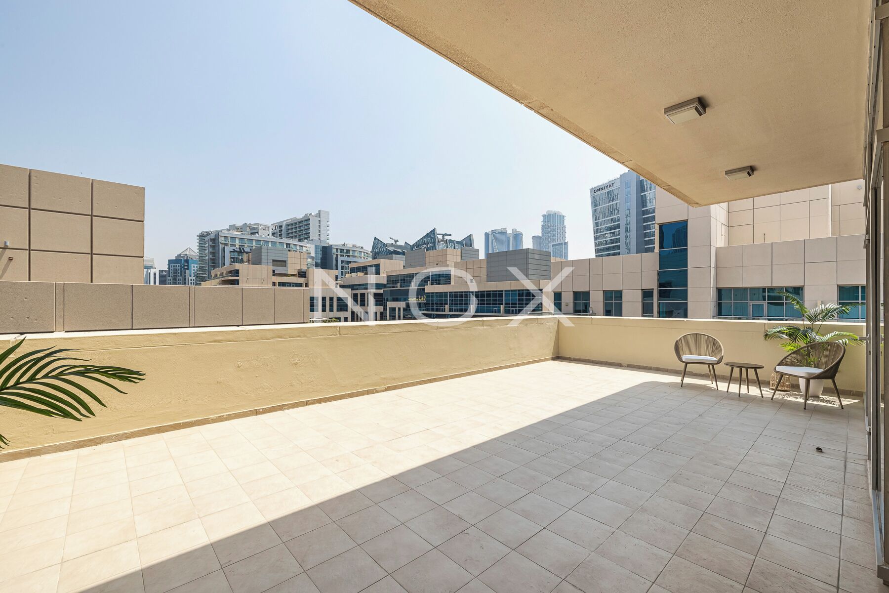 A rooftop terrace with a city view, tiled flooring, and a few chairs and a table.