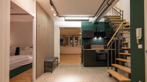 A compact living space with a bed, a bench, a kitchenette, and a staircase.