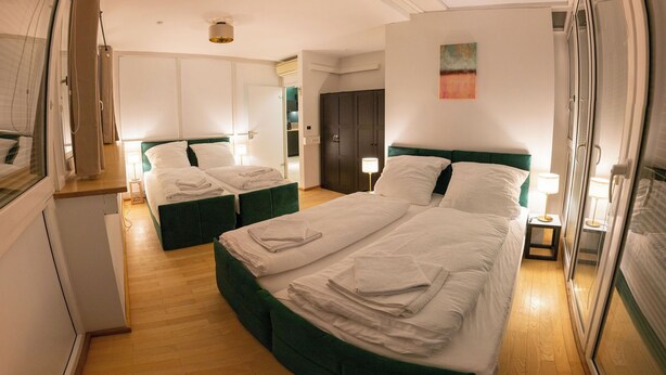 A hotel room with two beds, a wardrobe, and a small table with a lamp.
