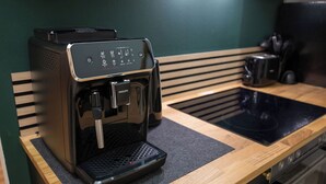 A coffee machine on a wooden countertop with a sink and stove in the background.