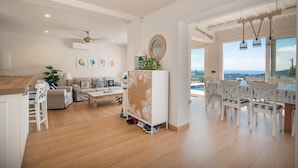 A spacious living area with a wooden floor, a sofa set, a dining table with chairs, a large mirror, and a view of the ocean. - Spacious 4 Bedroom Villa & Apartment Suite, Private Pool and Fantastic Views (Calonge)