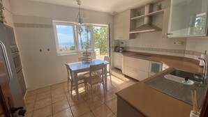 A kitchen with a dining table, a built-in oven, a sink, and a window with a view of palm trees. - Pura Vida, Casa con Preciosas Vistas una Piscina Maravillosa Ubicación Perfecta (Candelaria)