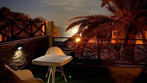An outdoor seating area with a table and chairs, a palm tree, and a fence. - Pura Vida, Casa con Preciosas Vistas una Piscina Maravillosa Ubicación Perfecta (Candelaria)