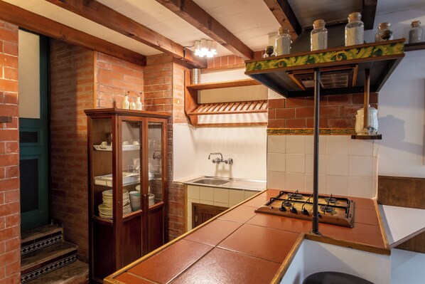 A kitchen with a brick wall, wooden cabinets, a sink, and a gas stove.