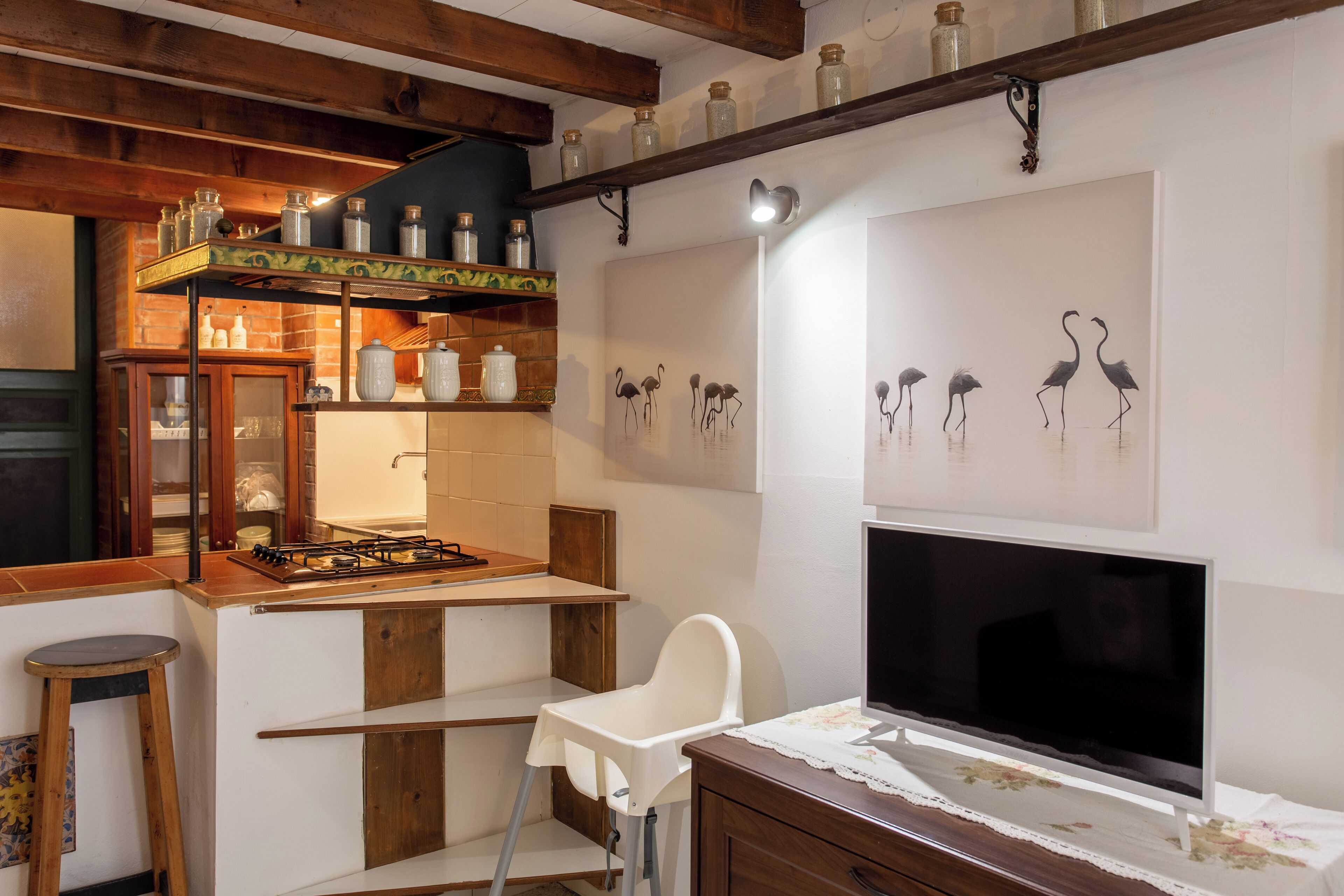 A kitchen with a gas stove, white chair, wooden cabinets, and a TV on the wall.