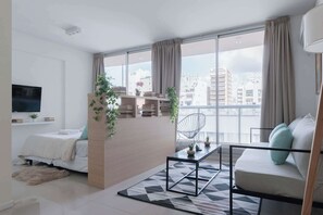 A modern living room with a sofa, a coffee table, a TV, and a balcony with plants.