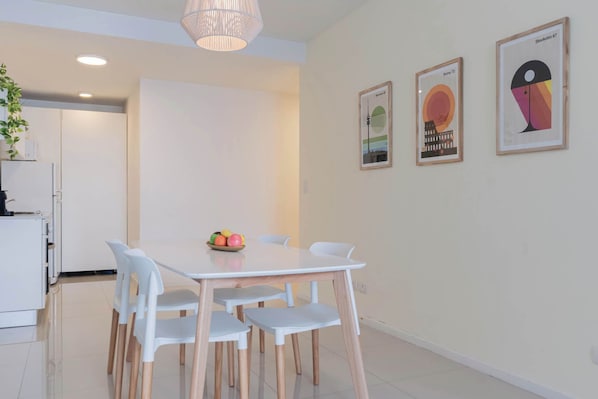 A modern dining area with a white table and chairs, a fruit bowl, and two framed artworks on the wall.