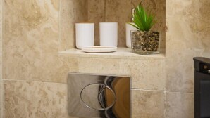 A bathroom with a marble wall, a shelf with toiletries, a small plant, and a metallic object. - Prime 3 Bedrooms Flat – Perfect for Families & Groups (Greater London)