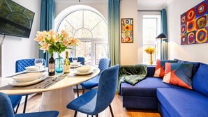 A modern living room with a blue sofa, a dining table set with plates, glasses, and a vase of flowers. - Prime 3 Bedrooms Flat – Perfect for Families & Groups (Greater London)