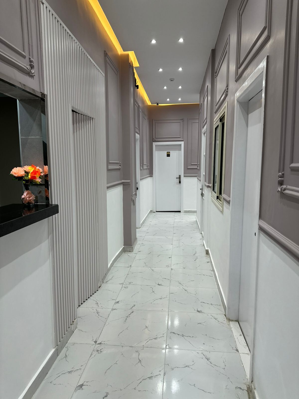A hallway with marble flooring, white walls, and a black reception desk with flowers.