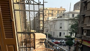 Een balkon met rieten meubilair, een metalen hekwerk en uitzicht op de straat.