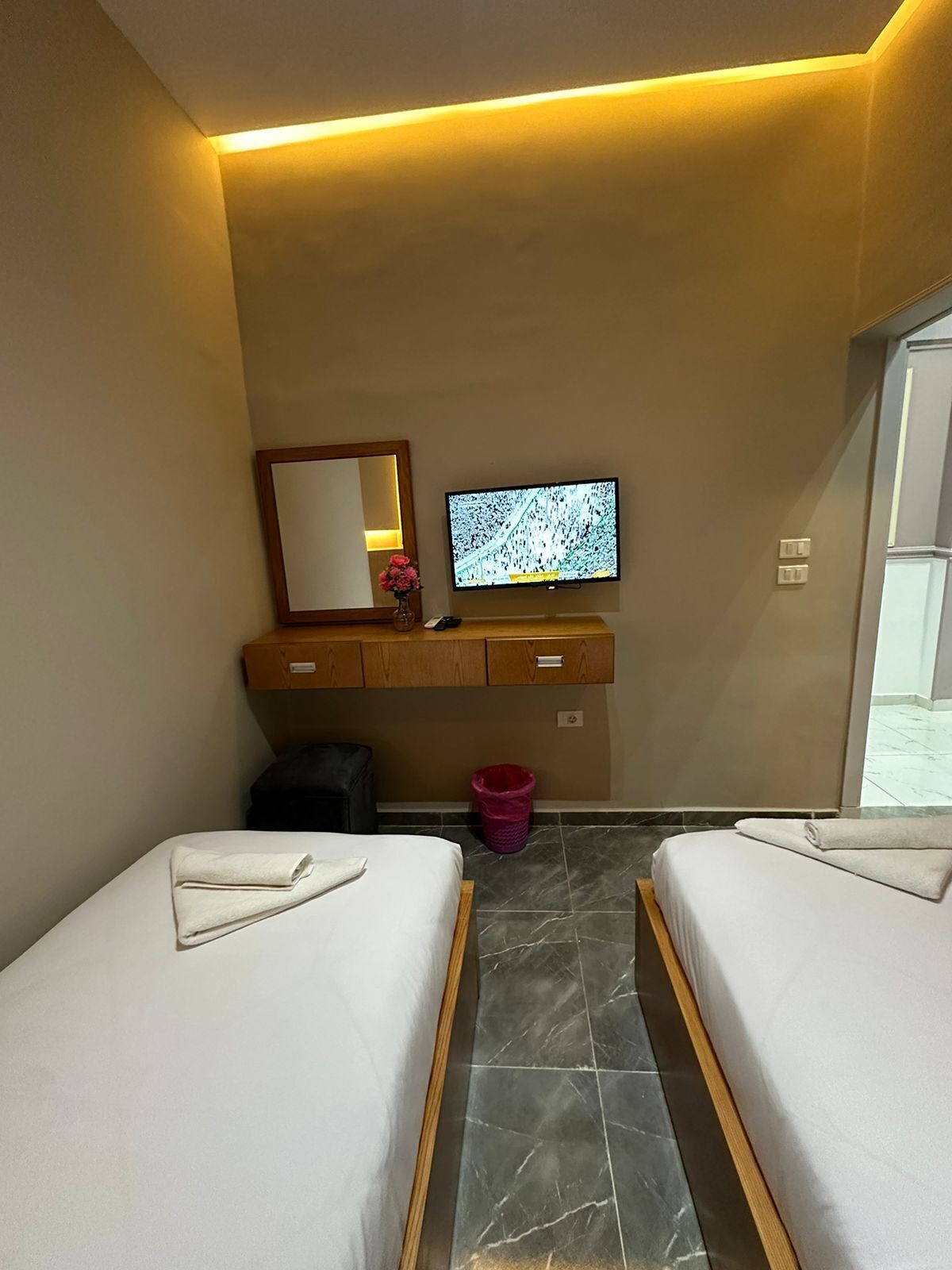 Une chambre d’hôtel avec deux lits, une télévision, un miroir, une petite poubelle et une armoire en bois.
