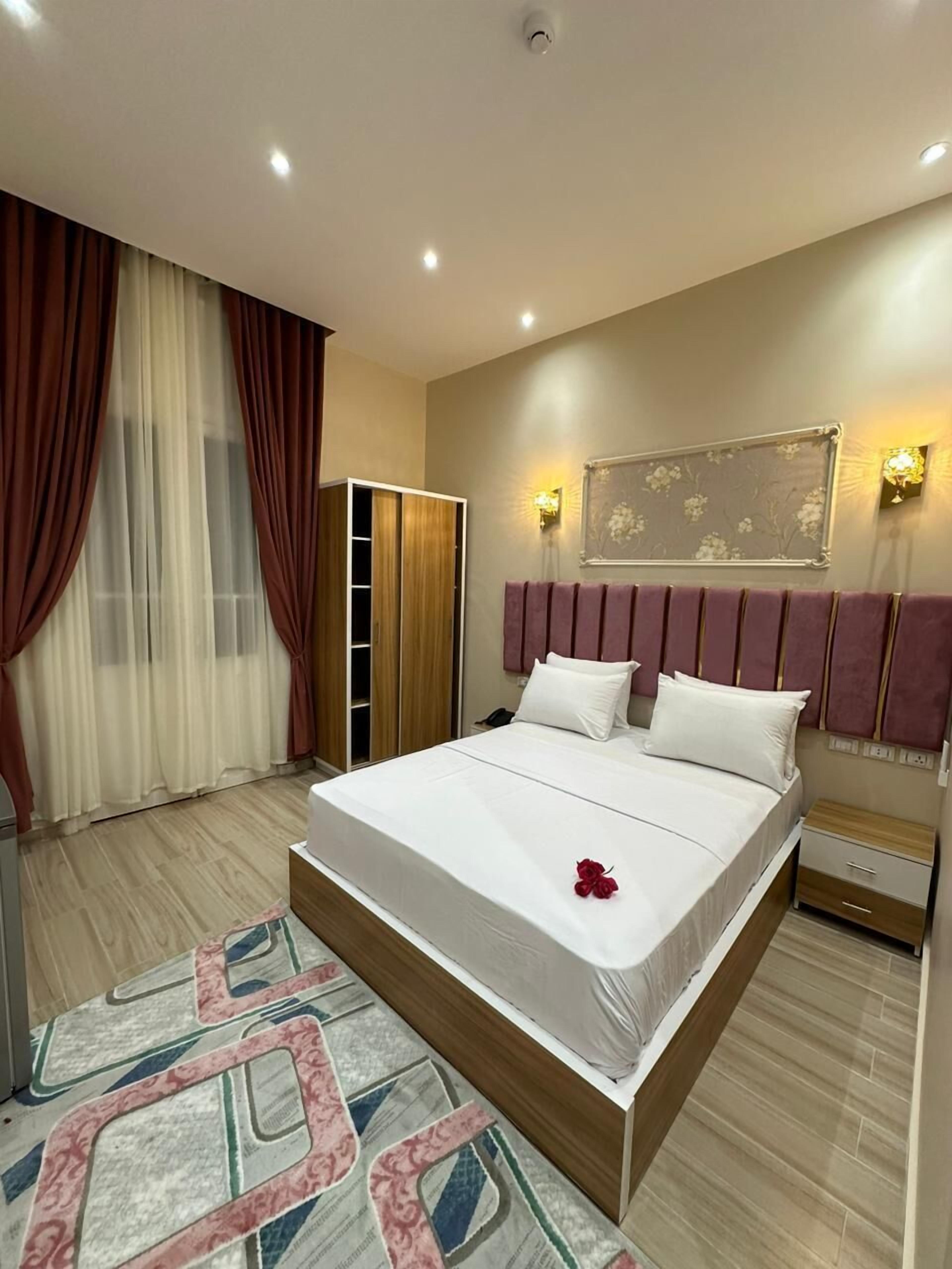 A modern hotel room with a large bed, a wardrobe, a bedside table, and a decorative wall panel.