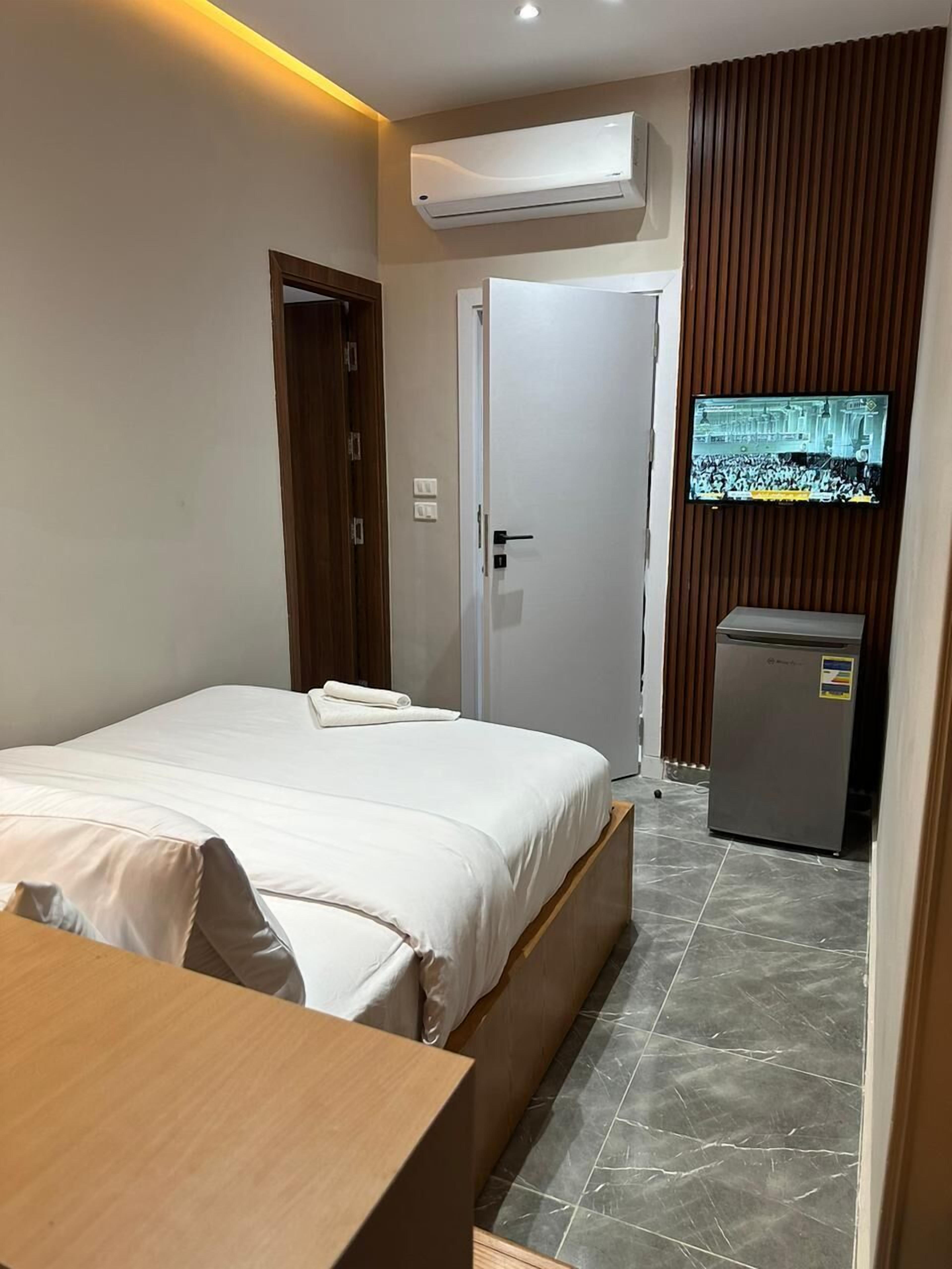 Une chambre d’hôtel équipée d’un lit, d’un téléviseur fixé au mur, d’un petit réfrigérateur et d’un bureau en bois.