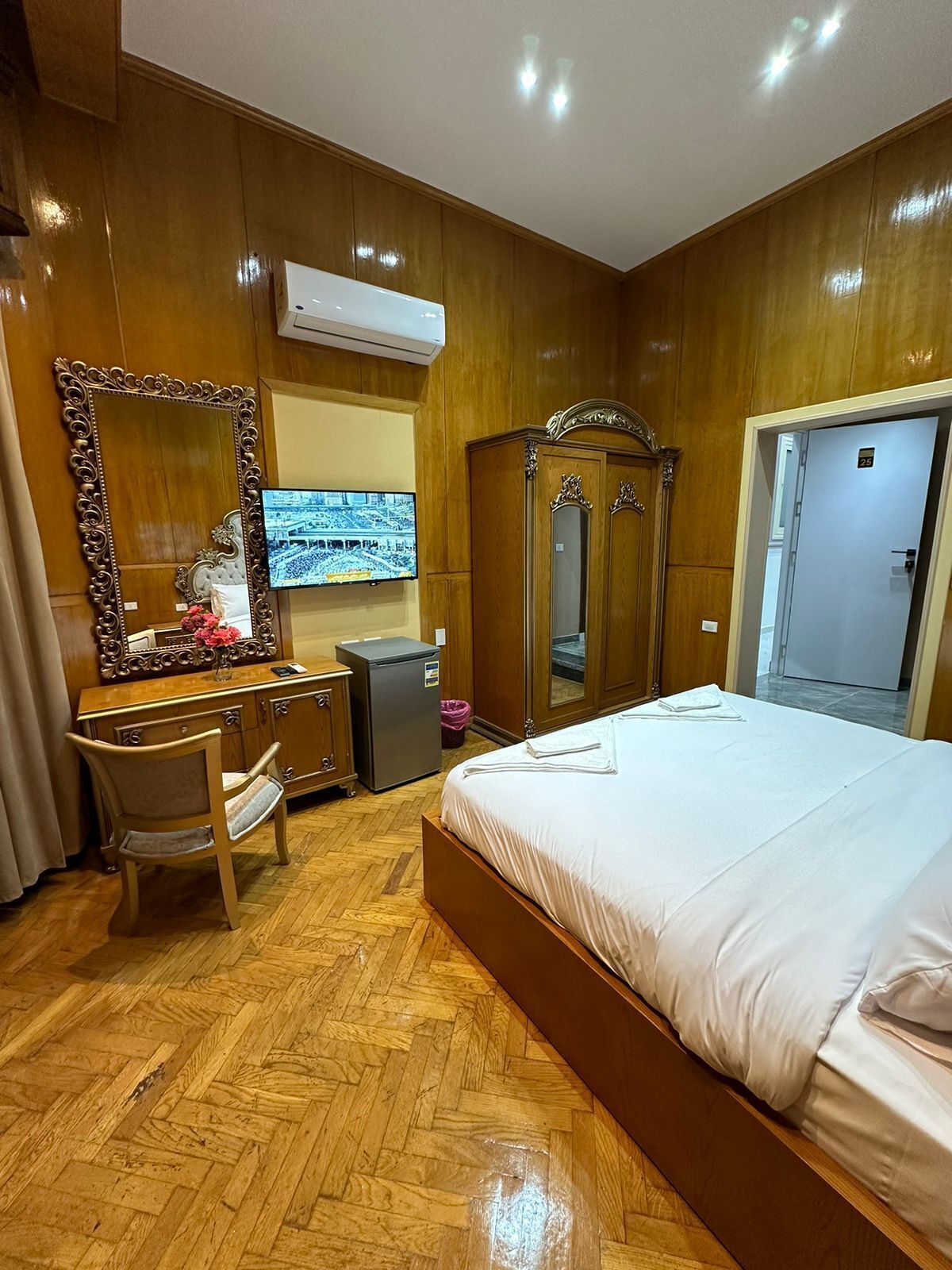 Habitación de hotel con piso de madera, una cama, un escritorio con silla, cómoda, espejo y televisión.