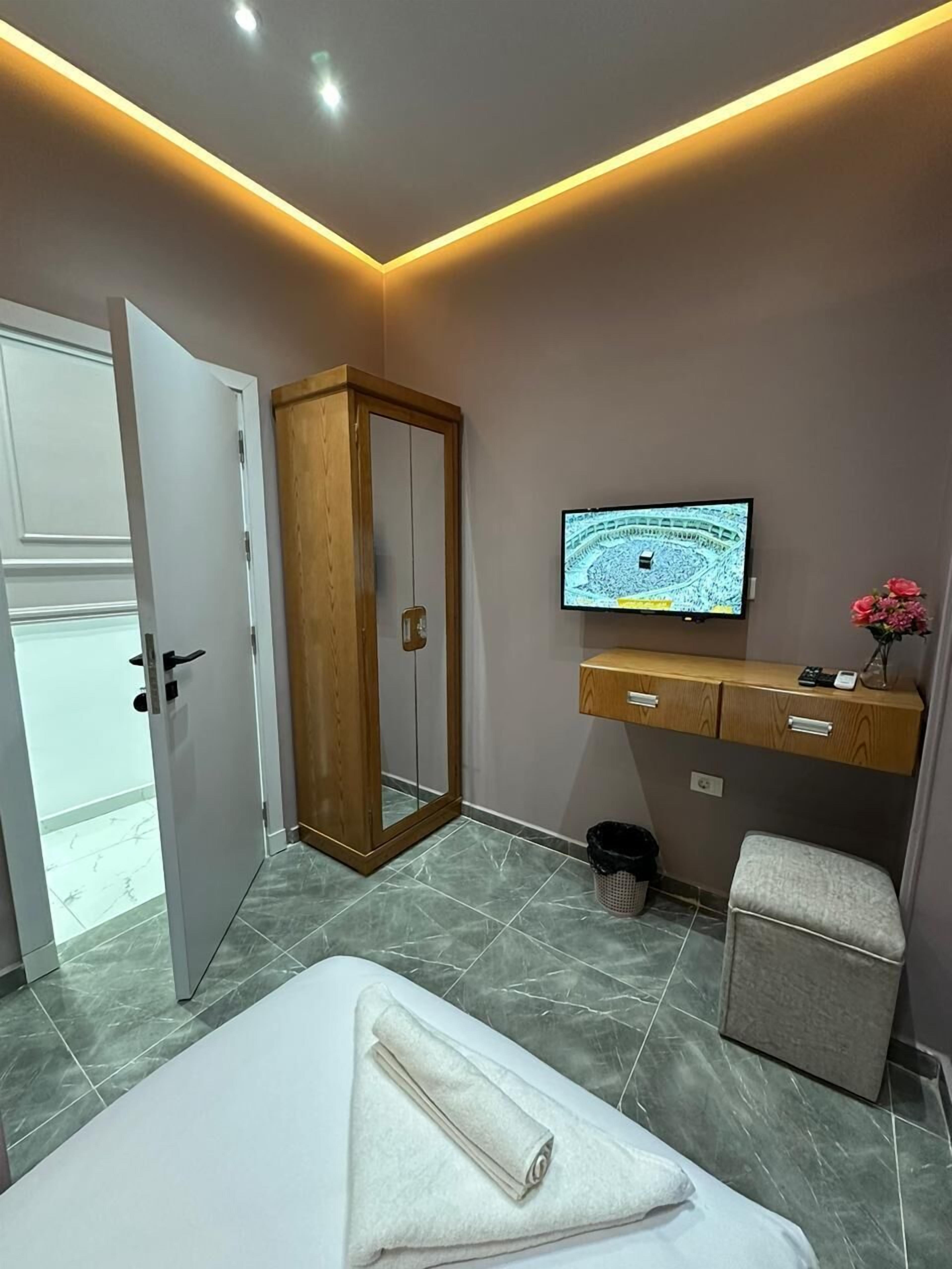 A modern bedroom with a bed, a wooden wardrobe, a television, and a small stool.