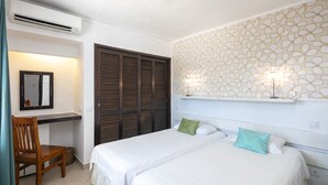 Ein Hotelzimmer mit zwei Betten, einem Schreibtisch, einem Sessel, einem Spiegel, einem Kleiderschrank und Wandtapete mit Muster.