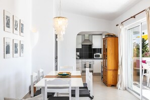 A modern kitchen with white cabinetry, a wooden cabinet, and a dining area with a table and chairs.