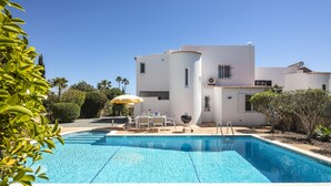 Ein Swimmingpool mit Terrassenbereich, ein weißes Gebäude und umliegendes Grün.