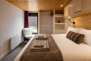 A bedroom with a bed, a chair, a wooden ceiling, and a window with curtains. - Stunning apartment with breathtaking view! (Huez)