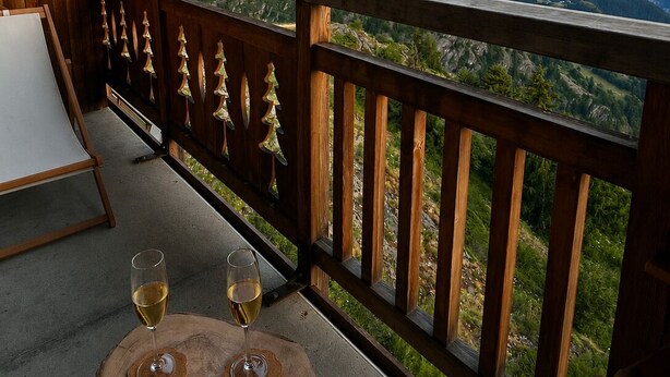 A wooden balcony with a table and two glasses of wine, overlooking a mountainous landscape. - Stunning apartment with breathtaking view! (Huez)