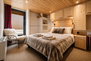 A modern bedroom with a large bed, wooden headboard, and a view of the outdoors. - Stunning apartment with breathtaking view! (Huez)
