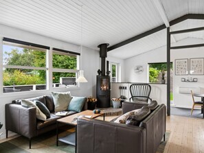 Ein modernes Wohnzimmer mit Kamin, Ledersofas, einem Couchtisch und großen Fenstern mit Blick auf Grünflächen.
