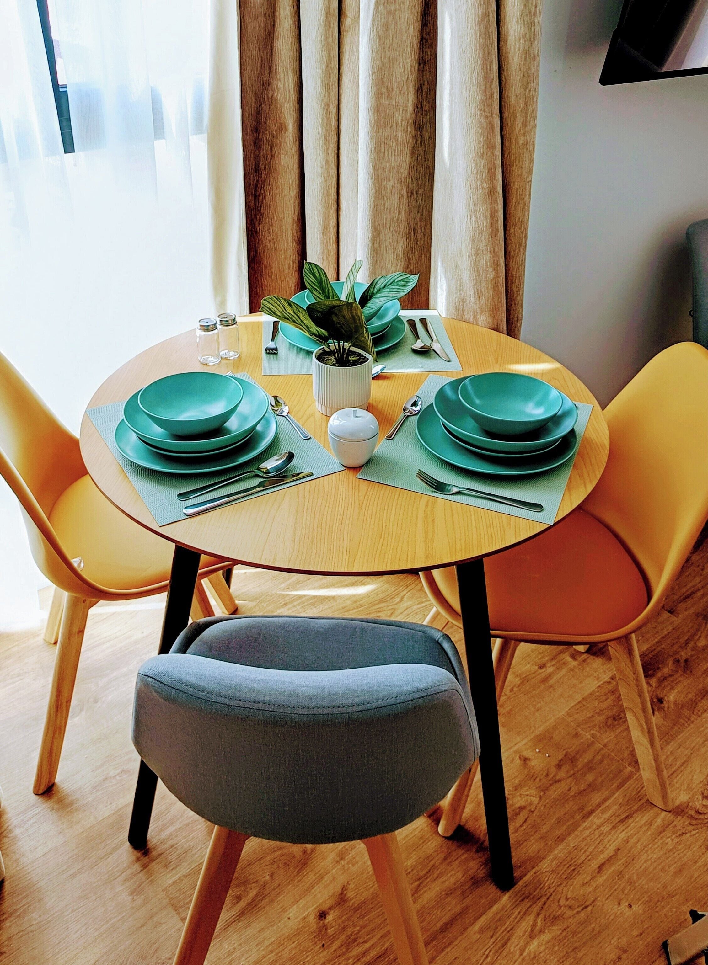 A round dining table with green plates, a white vase with a plant, and yellow chairs.