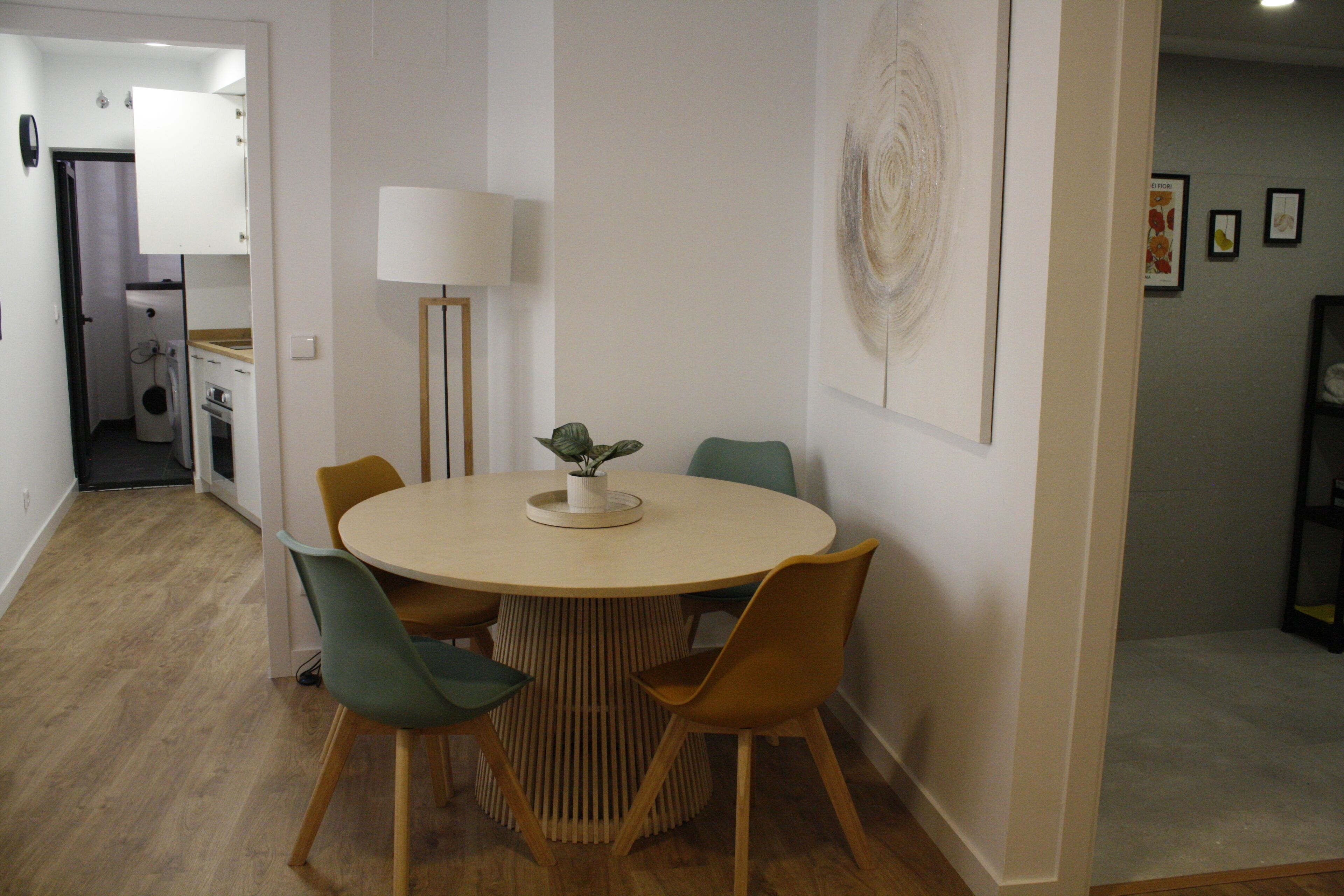 Comedor con una mesa redonda, cuatro sillas, una lámpara y una obra de arte colgada en la pared.