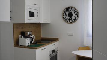 Una cocina compacta con armarios blancos, encimera de madera, cafetera y un reloj de pared.