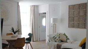 Un salon moderne avec une table à manger ronde, des chaises vertes, un canapé agrémenté de coussins à motifs et une petite table d’appoint.