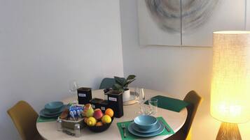 A dining area with a round table, chairs, a fruit bowl, plates, cutlery, and a lamp.