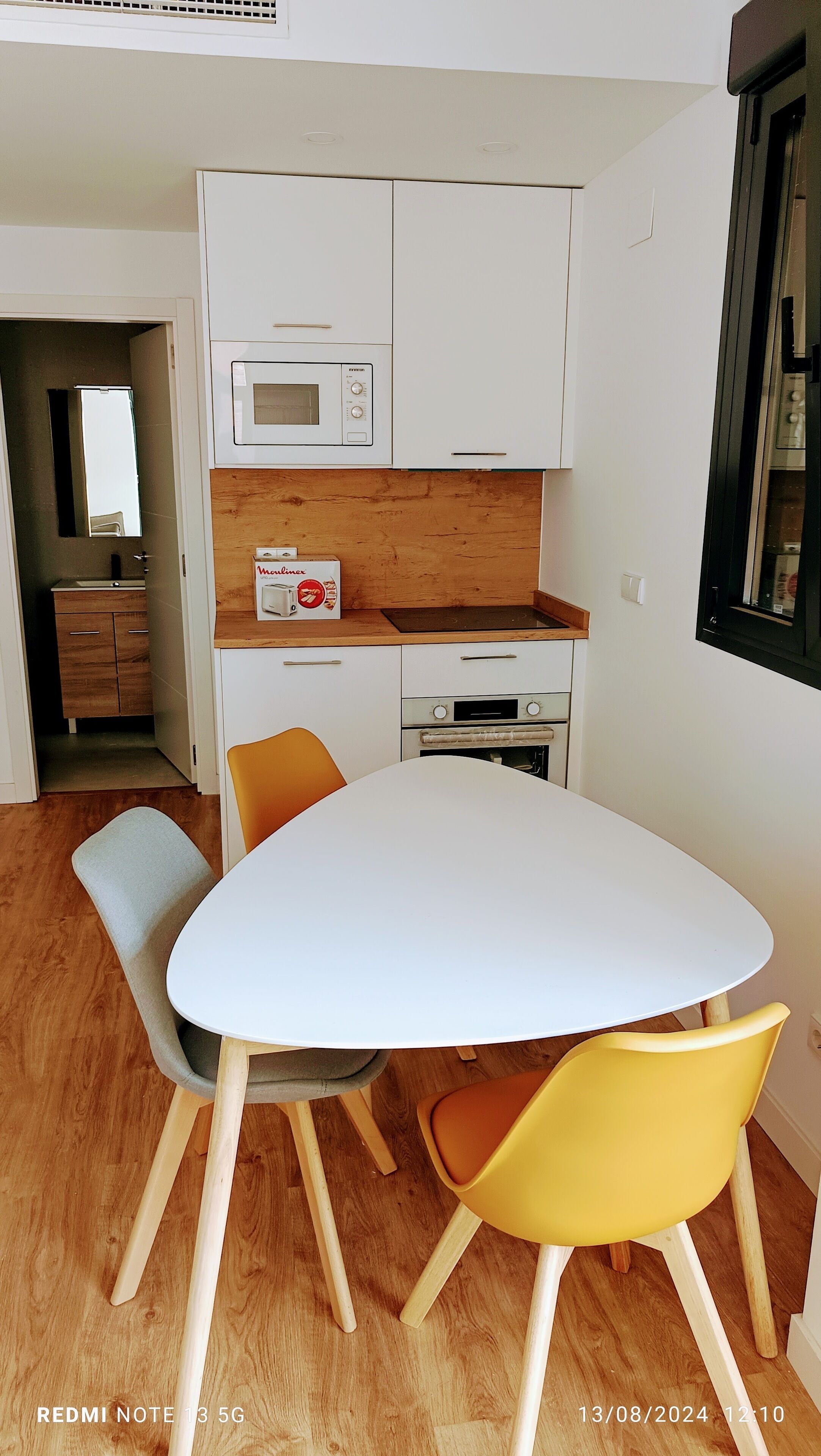 Una cocina moderna con armarios blancos, un microondas, una estufa y una mesa de comedor con dos sillas.