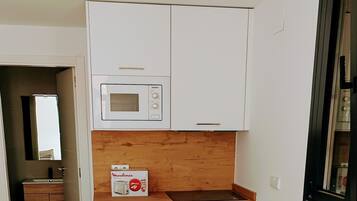 Una cocina moderna con armarios blancos, un microondas, una estufa y una mesa de comedor con dos sillas.