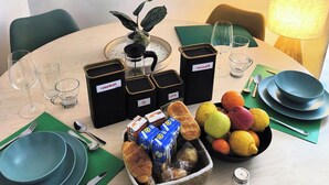 Uma mesa de jantar posta com pratos, copos, uma cafeteira e uma fruteira.