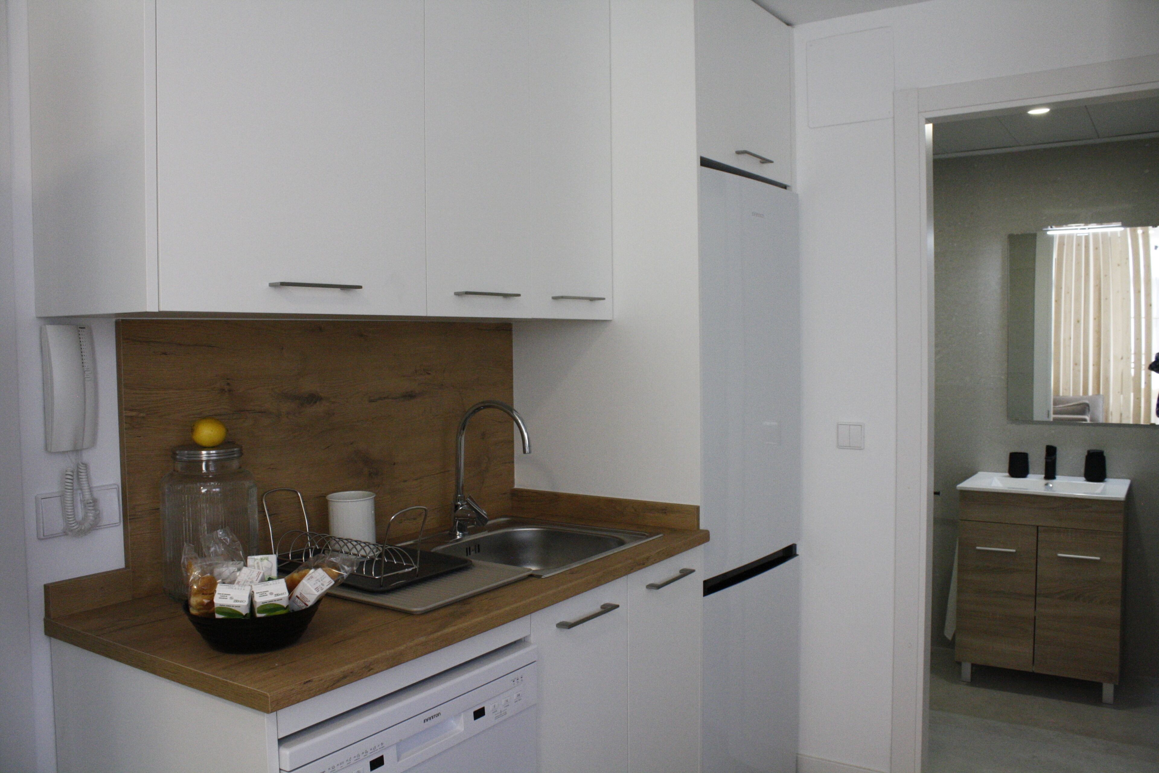 Una cocina moderna con armarios blancos, encimera de madera, un lavamanos y un lavavajillas.