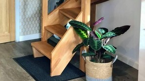 Un escalier en colimaçon en bois, doté d’une rampe métallique, mène à un palier où se trouve un pot de fleurs.