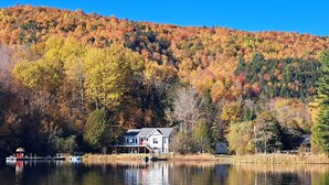 Une maison au bord d’un lac, avec le feuillage automnal en arrière-plan.