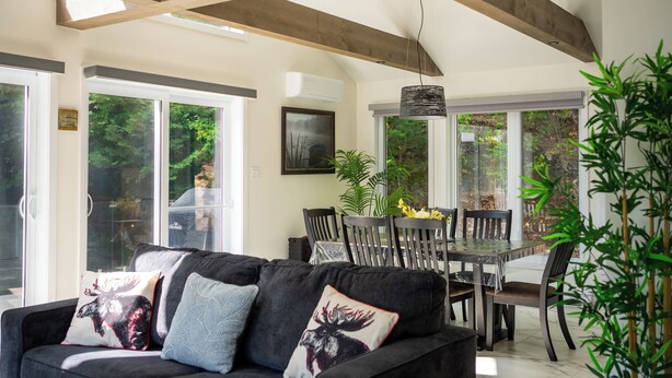 Un salon moderne avec un canapé foncé, une table à manger avec des chaises et une grande fenêtre donnant sur un paysage verdoyant.