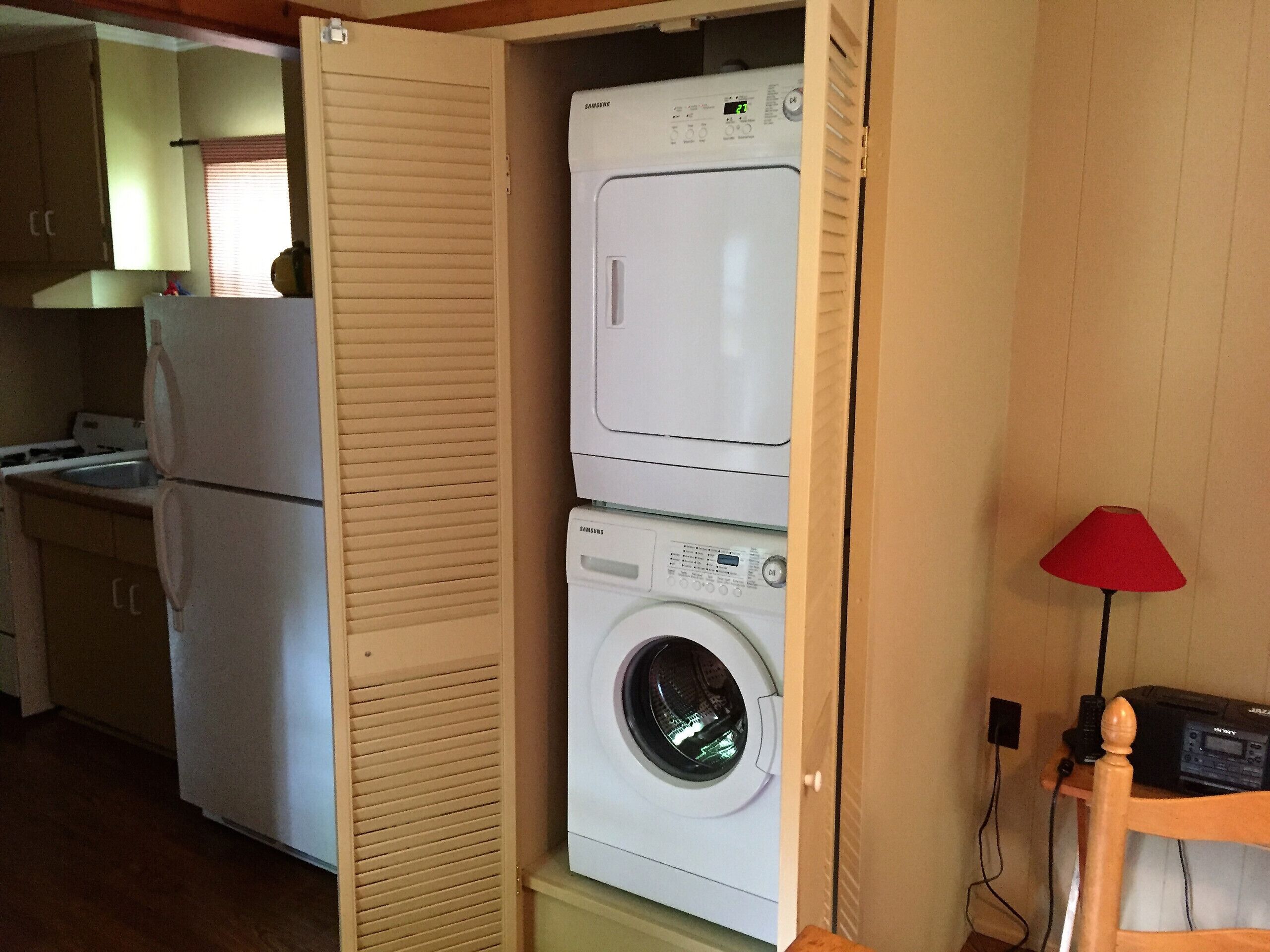 Une cuisine compacte équipée d’un lave-linge et d’un sèche-linge intégrés, d’un meuble en bois et d’une petite table avec une lampe.