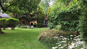 En frodig have med græsplæne, hvide stole og mange forskellige planter og blomster.