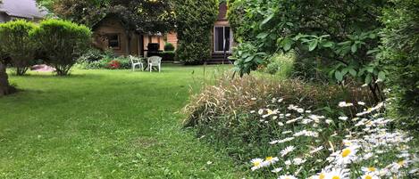 Un jardin luxuriant avec une pelouse, des chaises blanches et une grande variété de plantes et de fleurs.