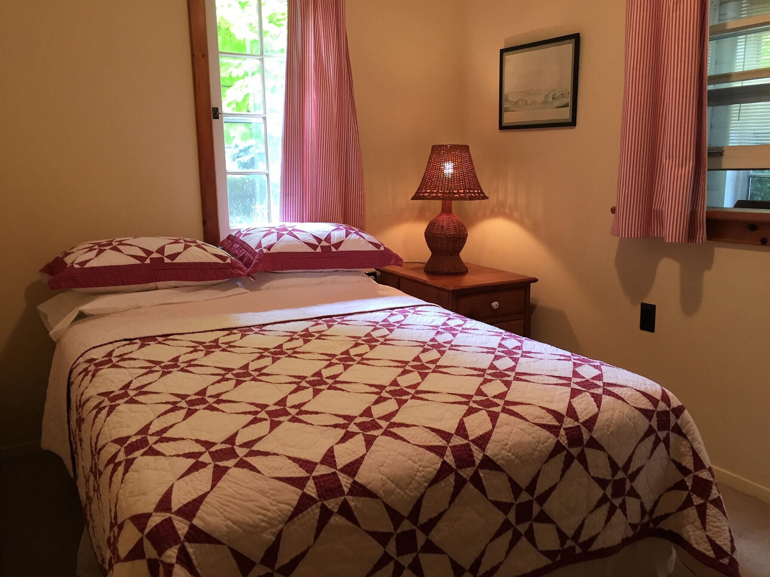 Une chambre à coucher avec un lit, des oreillers, une table de chevet, une lampe et une fenêtre avec des rideaux.