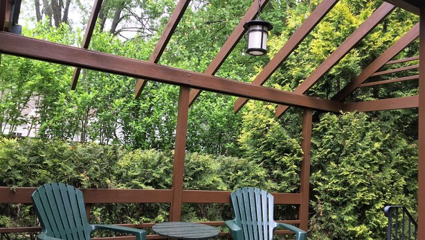 En træterrasse med to grønne Adirondack-stole og et lille bord, omgivet af frodig grøn vegetation.