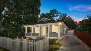 A two-story house with a porch, a white picket fence, and a driveway leading to a garage. - Historic St Augustine | Courtyard Fireplace | Dog Friendly (St. Augustine Beach)