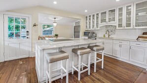 A kitchen with a central island, white cabinetry, and a wooden floor. - Historic St Augustine | Courtyard Fireplace | Dog Friendly (St. Augustine Beach)