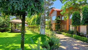 A well-maintained garden with a gazebo, a paved pathway, and a modern building with large windows. - Saraswatipur Tea resort (Jalpaiguri)