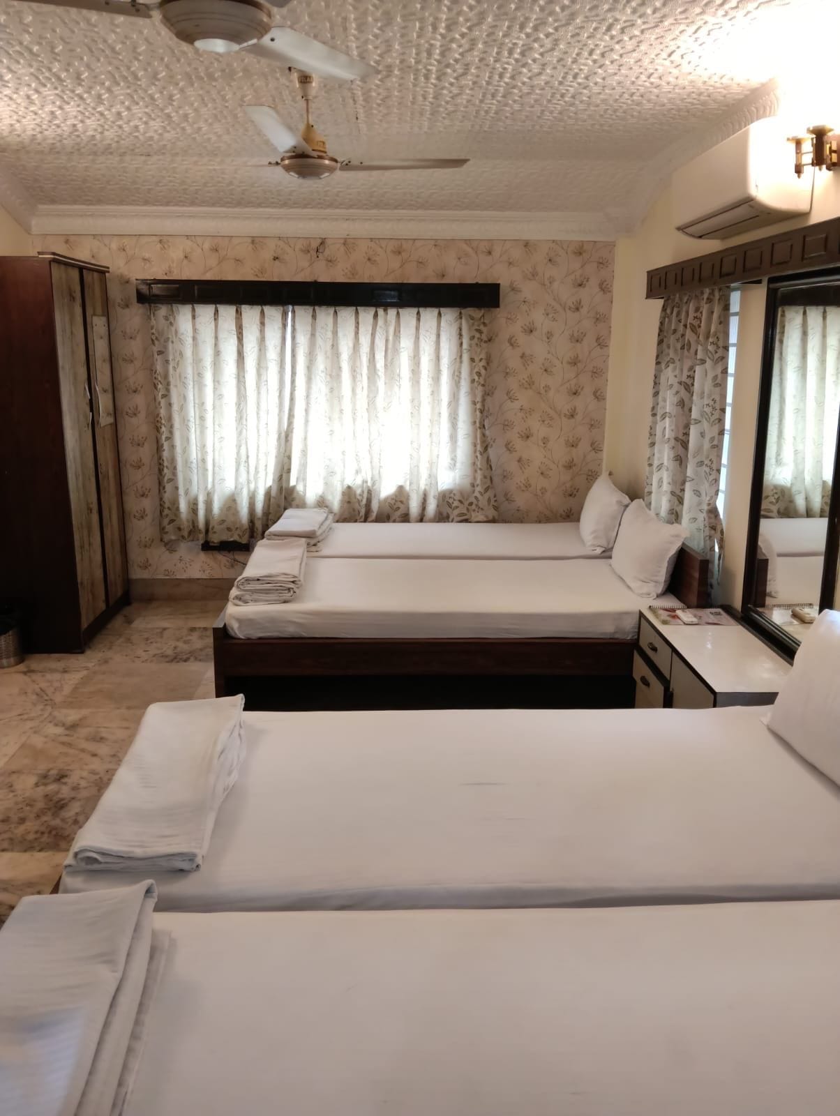 Quarto de hotel com duas camas, um ventilador de teto e uma janela com cortinas.