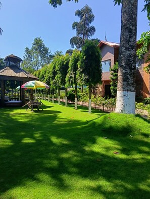 Ein gepflegter Garten mit einem Gartenpavillon, einem Esstisch und Stühlen unter einem bunten Sonnenschirm.